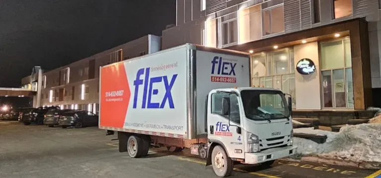 Camion de déménagement Flex stationné le soir devant un immeuble, avec des bancs de neige en bordure du stationnement
