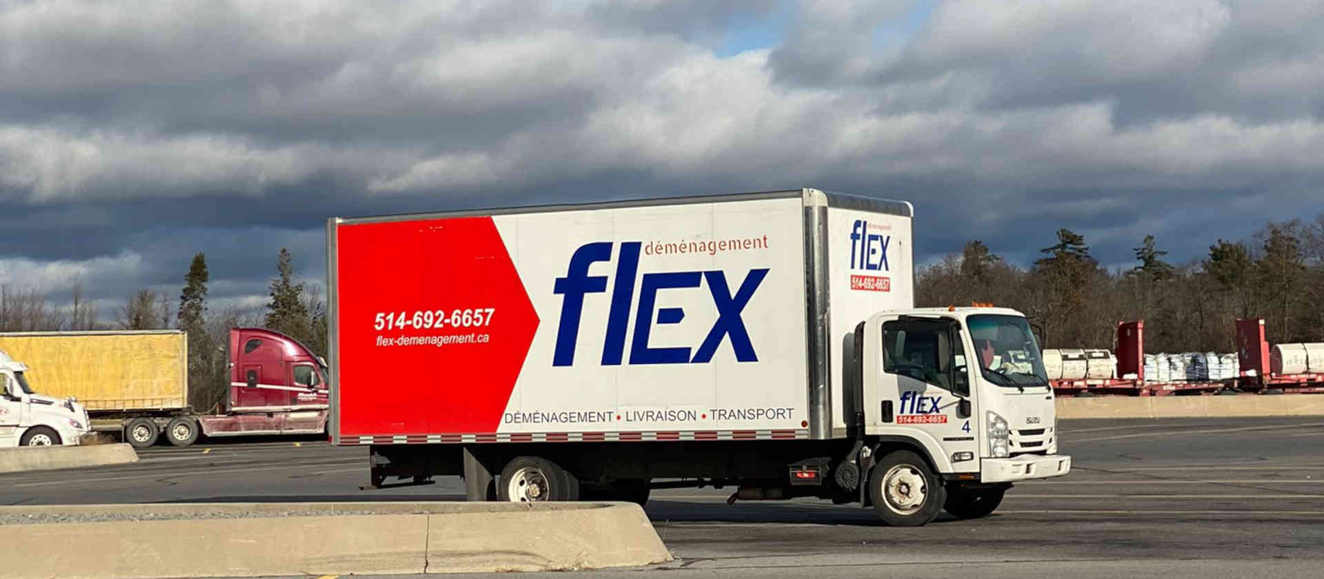 Camion de Flex Déménagement stationné dans une cour de transport à côté de semi-remorques, prêt pour la route vers Québec