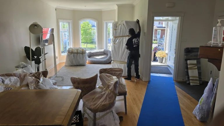 Déménageur Flex dans un salon, meubles emballés dans du plastique et tapis de protection posé jusqu'à la porte avant le chargement